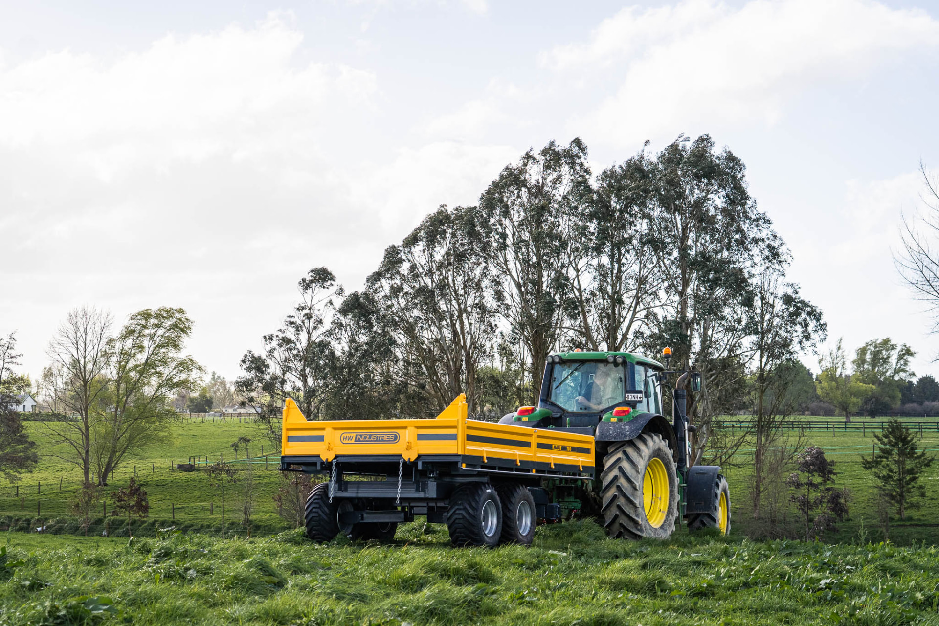 Yellow Maxi tip trailer behind a John Deere tractor in a green New Zealand paddock