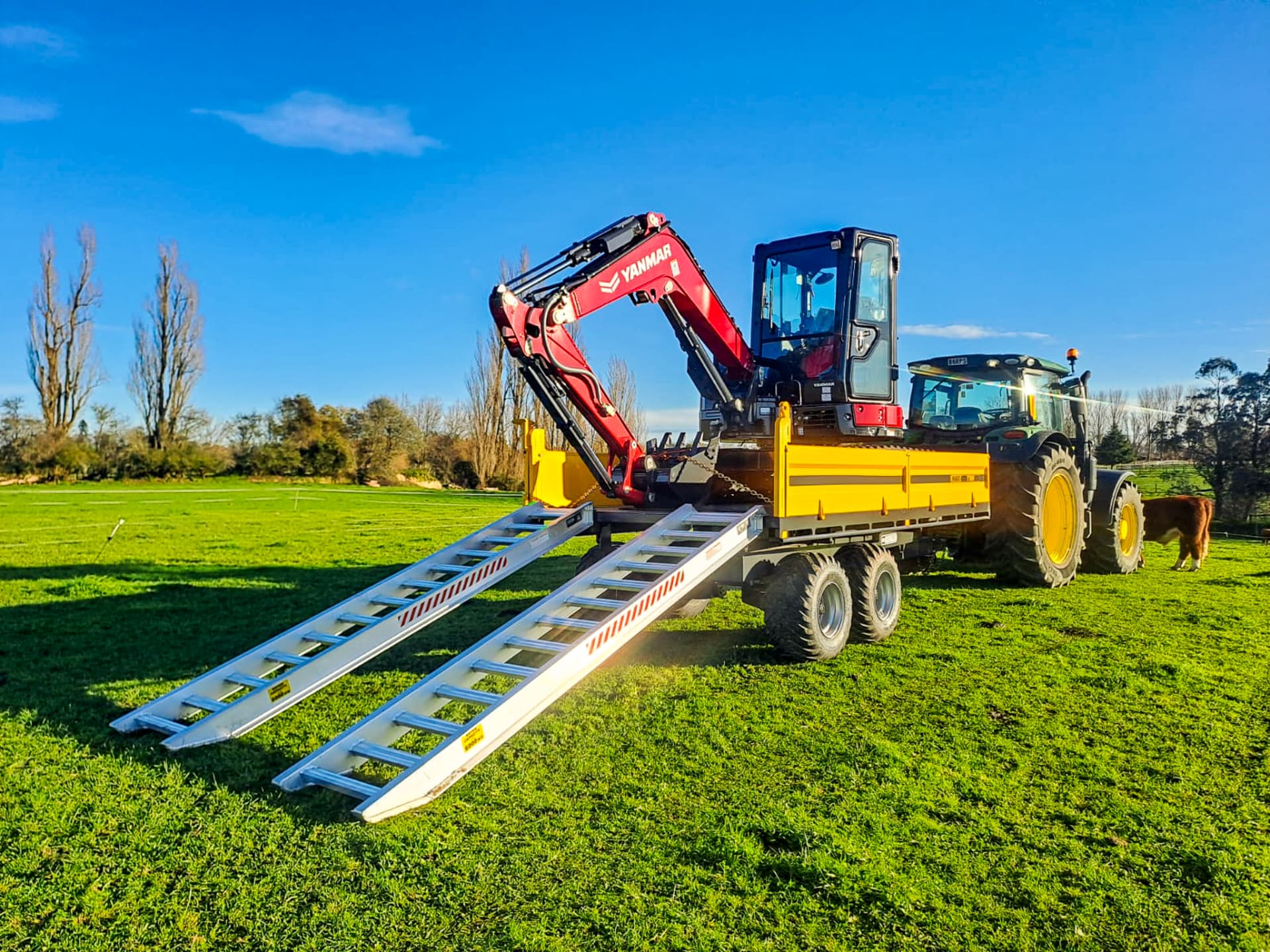 Maxi tip trailer carrying a Yanmar digger with loading ramps on a farm