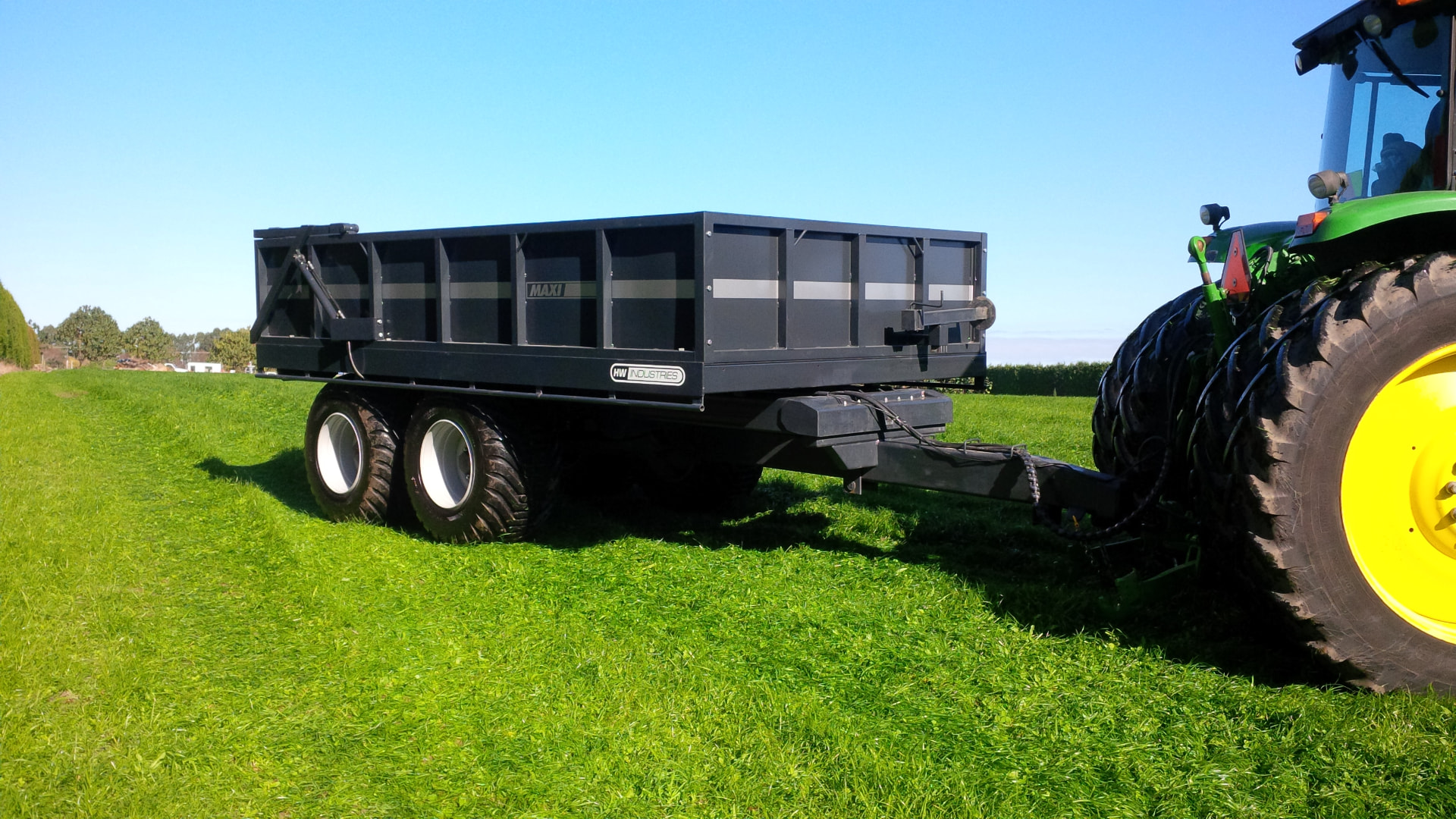 Black Maxi tip trailer behind a John Deere tractor in a green paddock