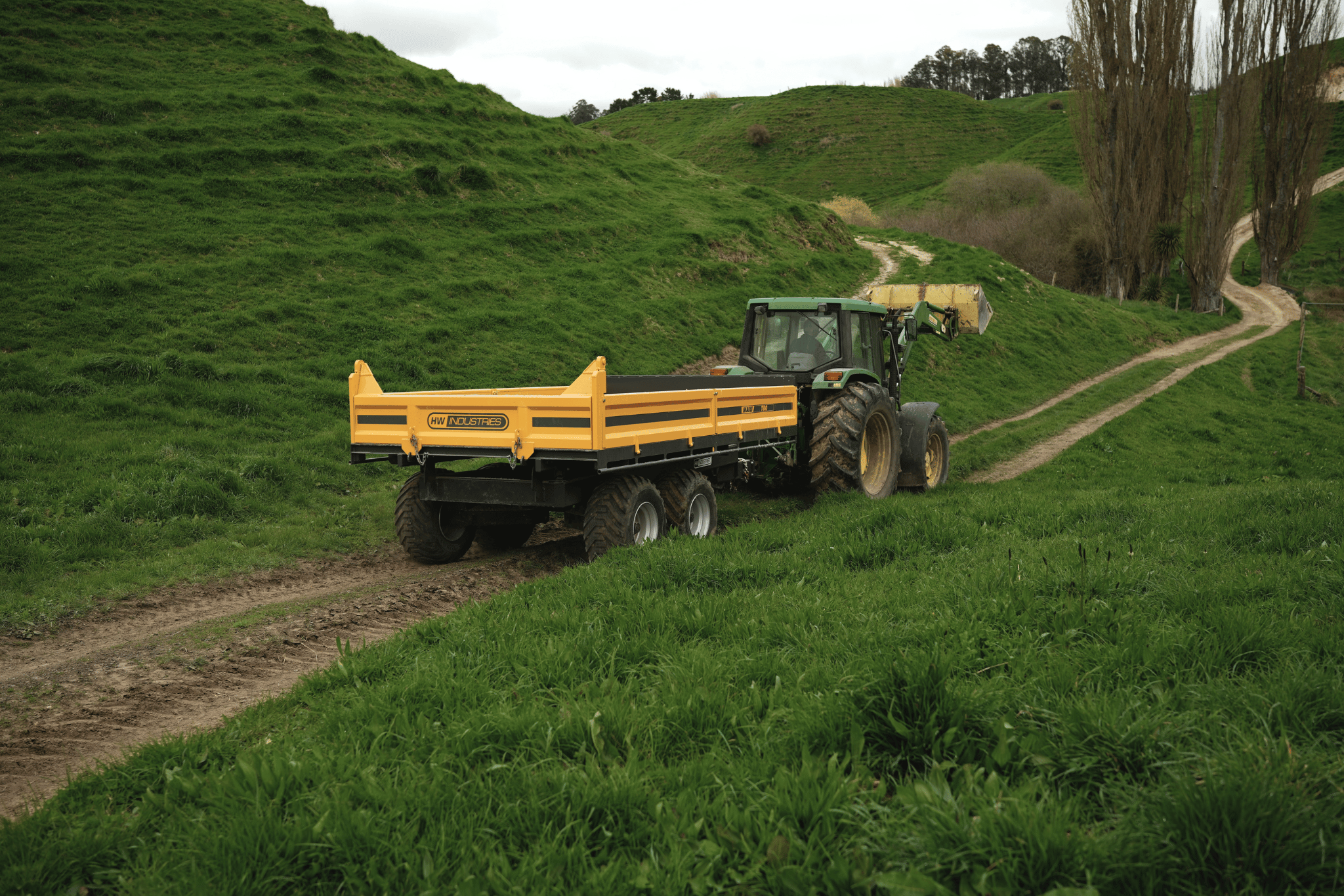 Tractor and Maxi tip trailer heading down a farm track through grassy hill country