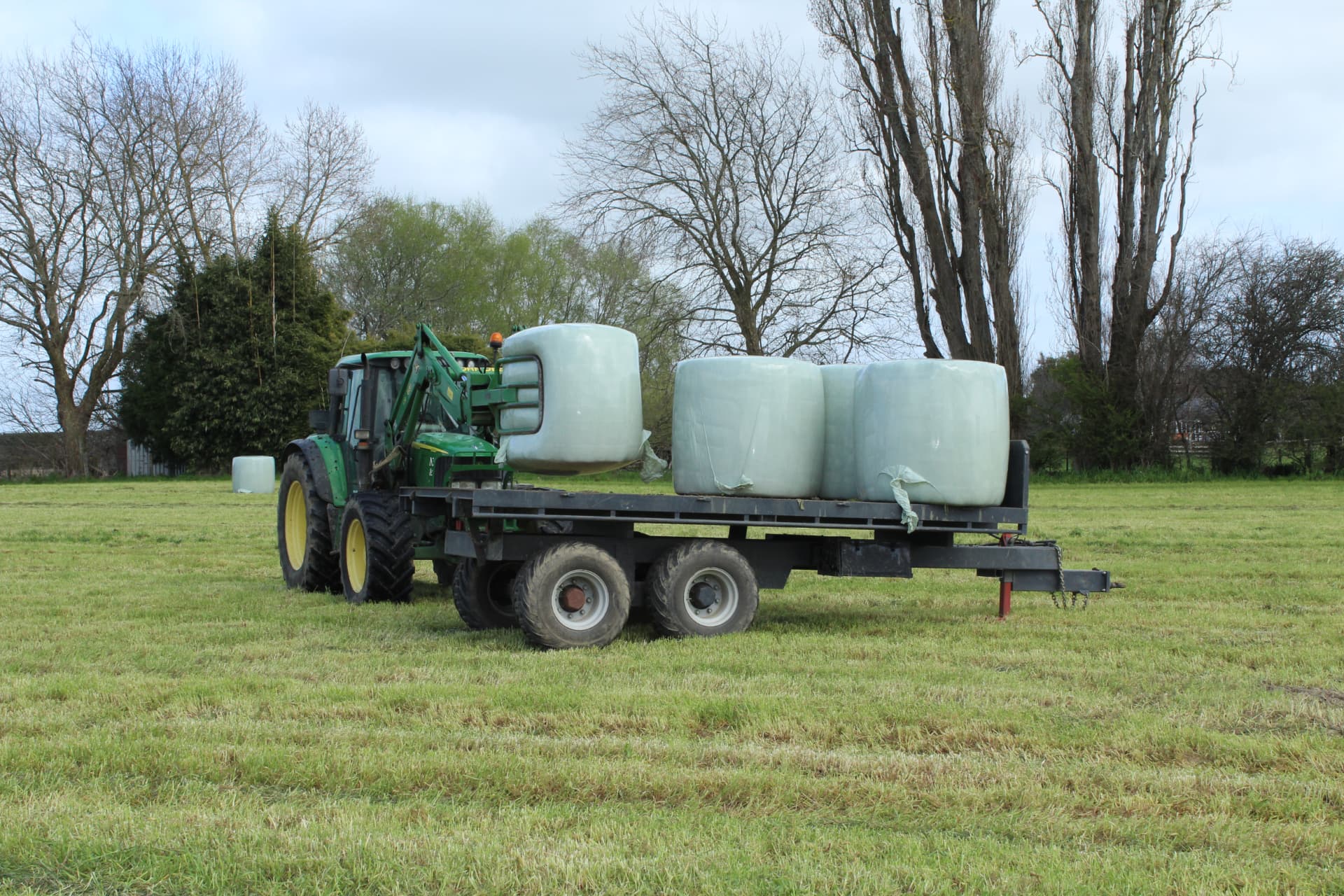 John Deere loader placing wrapped silage bales onto a Maxi flat-deck trailer in a paddock