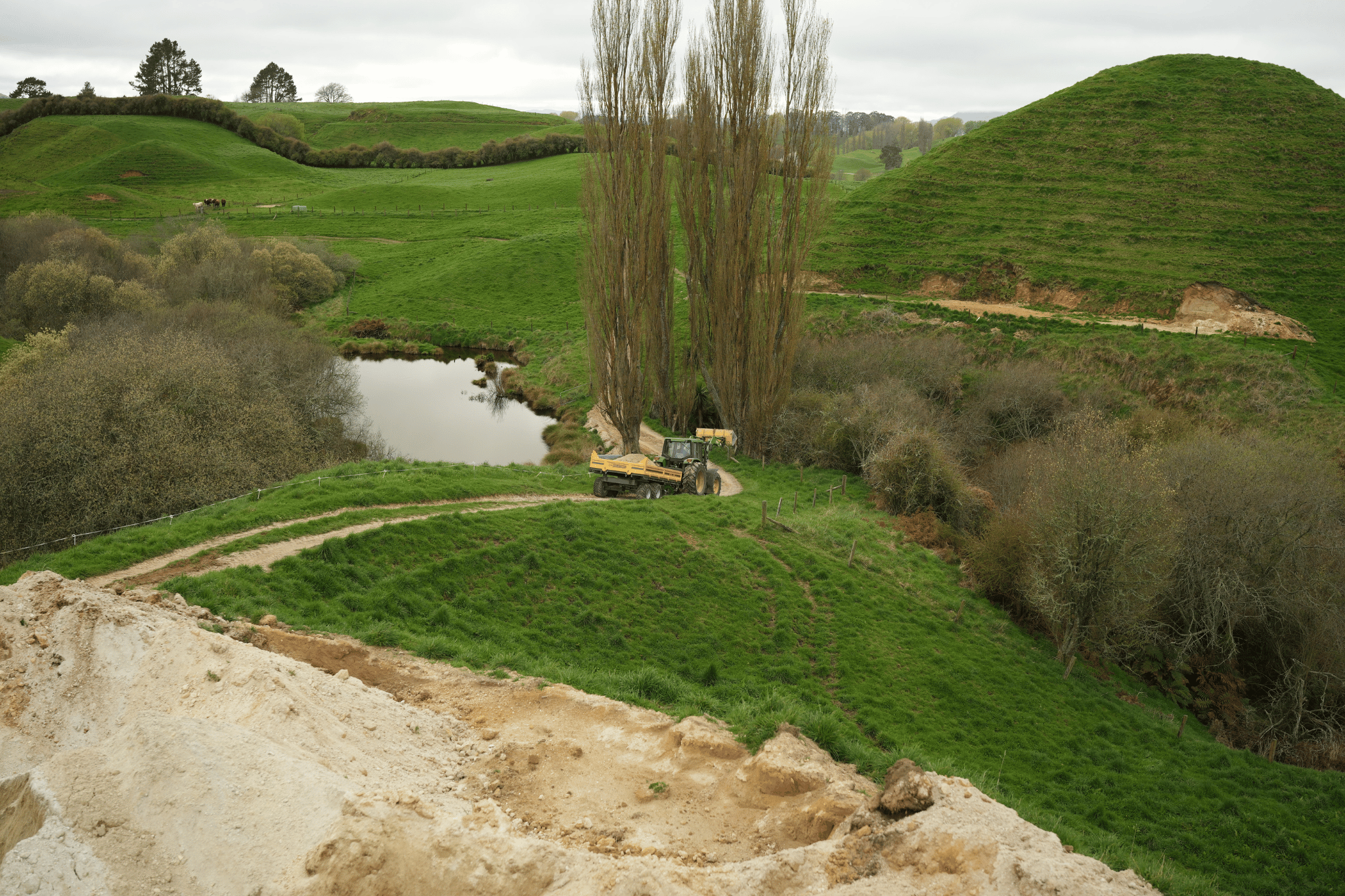 Aerial view of a loaded Maxi trailer travelling a winding farm track past a pond and fill site